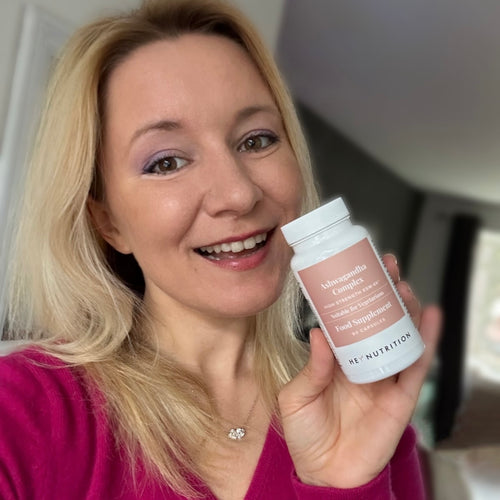 Woman smiling and holding a bottle of Hey Nutrition Ashwagandha Complex in her right hand.