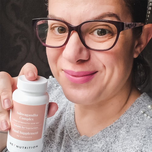 Woman with glasses smiling slightly while holding a bottle of Hey Nutrition Ashwagandha Complex.