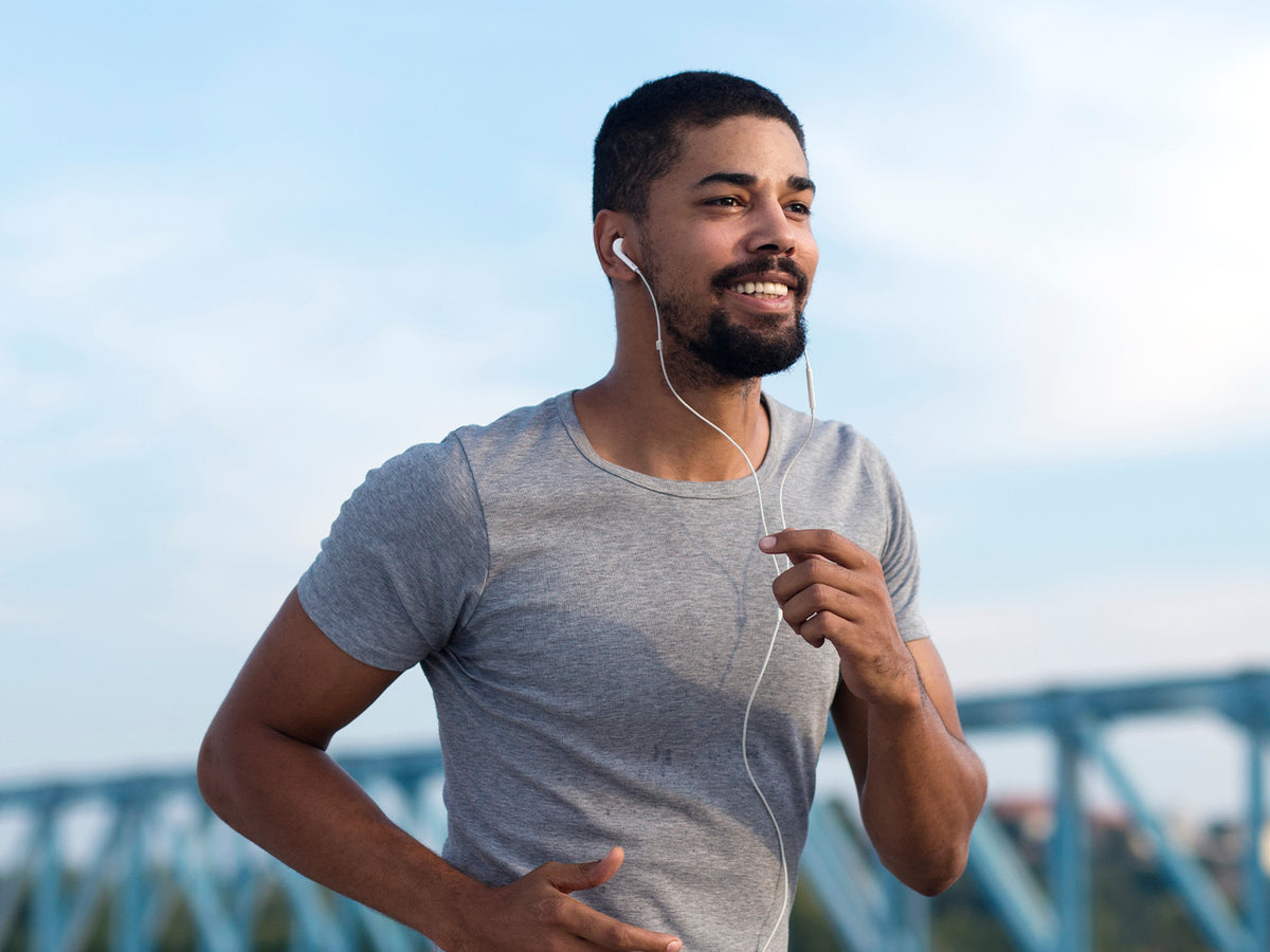 Man jogging outdoors in a grey t-shirt with earphones, looking happy and energized.