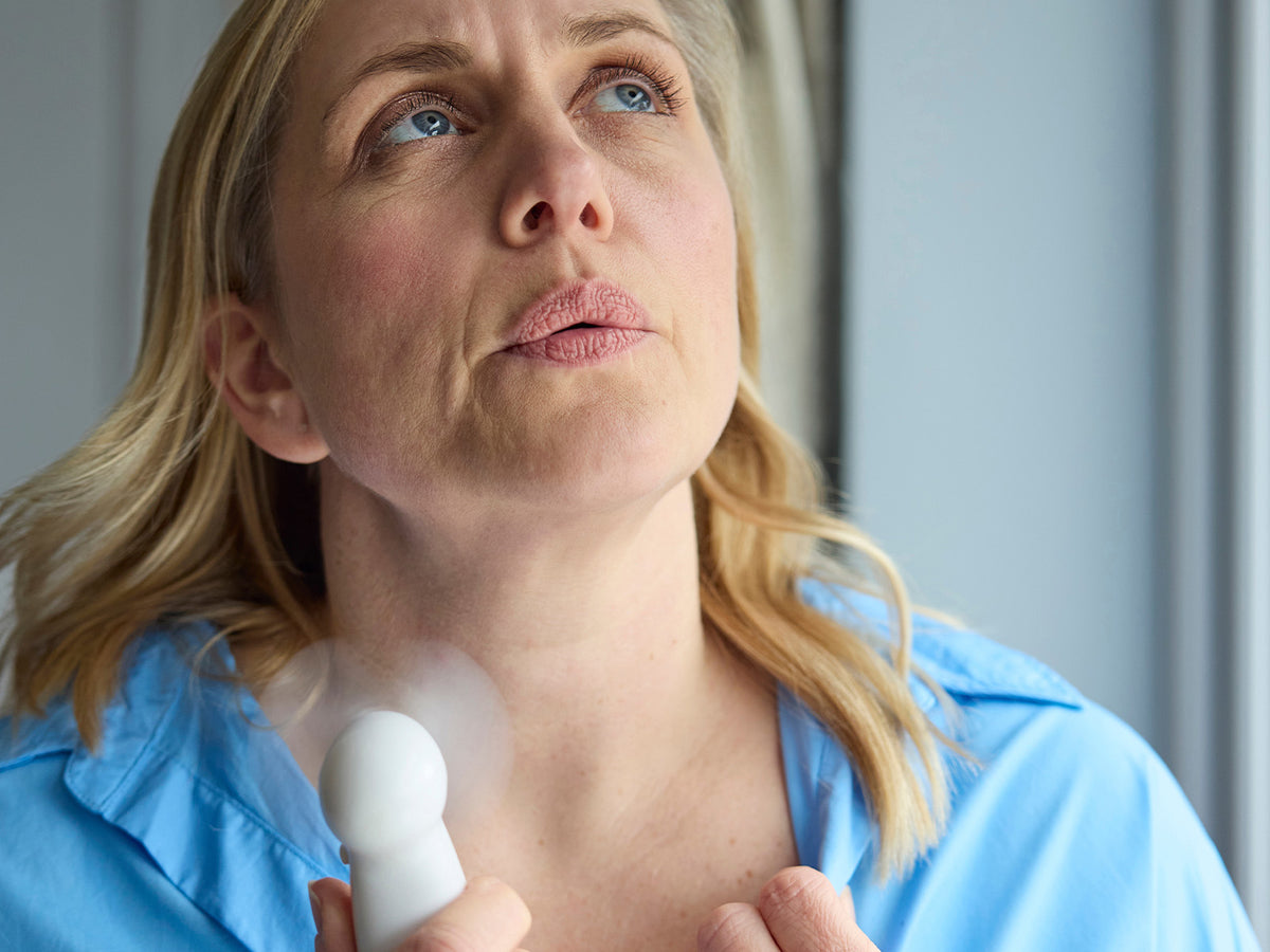 Middle-aged woman cooling herself with a handheld fan, looking up