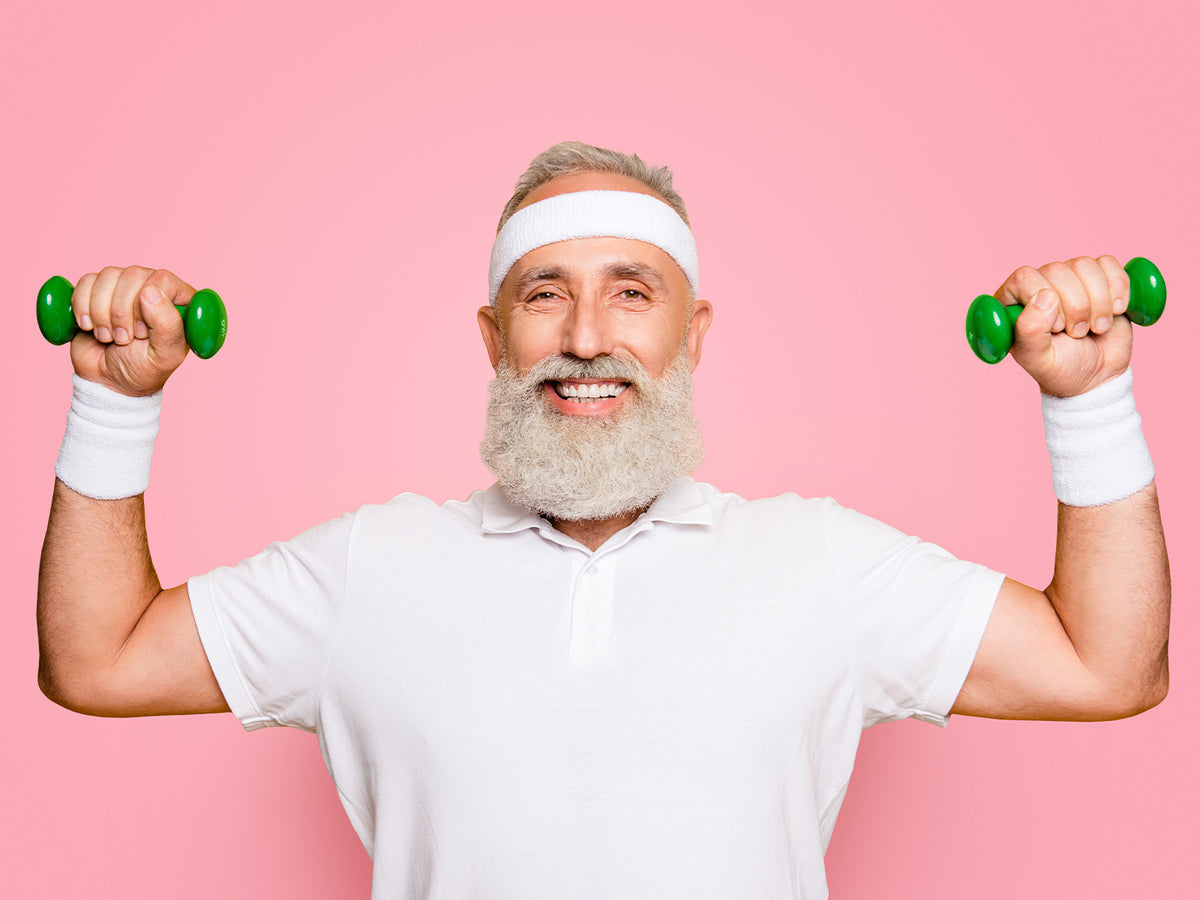Older man lifting green dumbbells and smiling, representing strength and vitality supported by Vitamin D3 and K2.