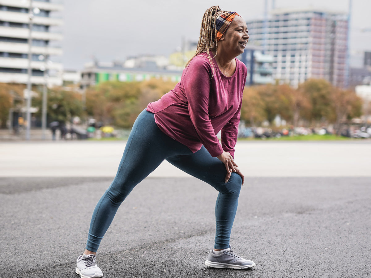 Woman stretching outdoors with hand on knee during warm-up