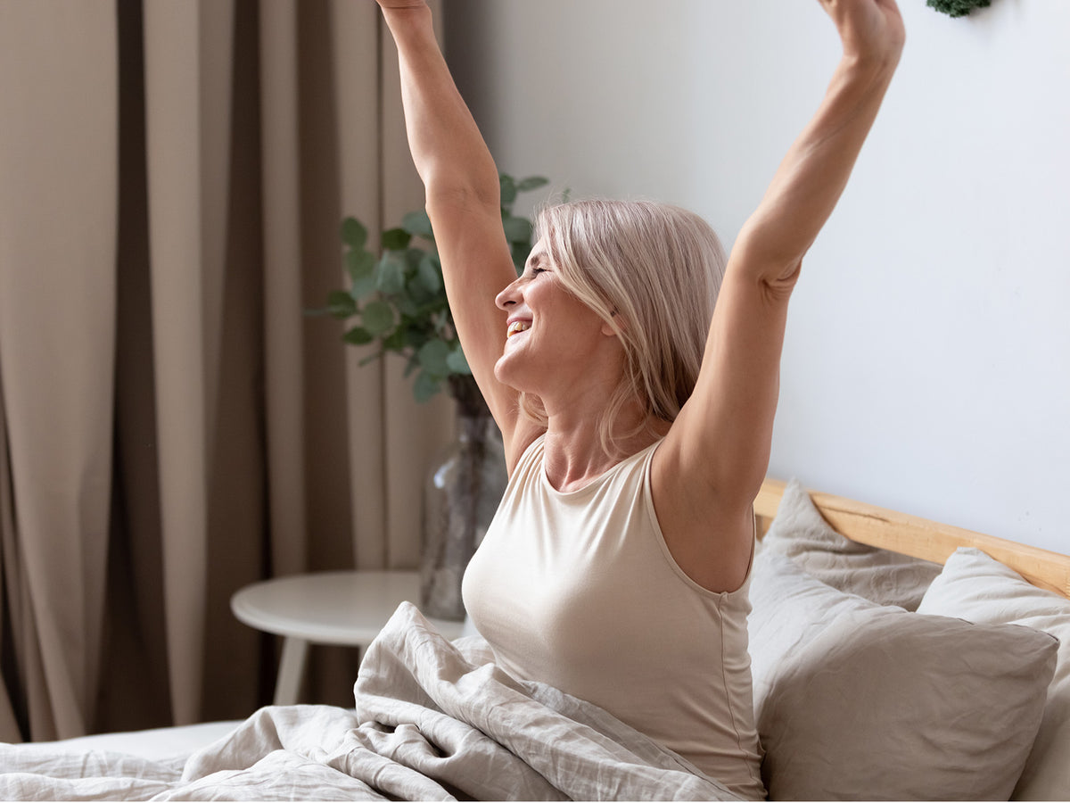 Smiling woman stretching arms after waking up in bed