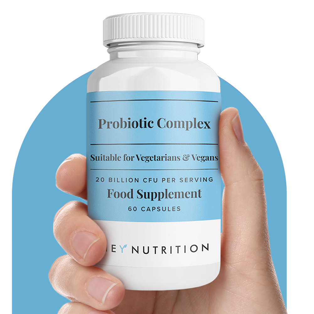 Close-up of a hand holding a Hey Nutrition Probiotic Complex food supplement bottle against a blue background, showing label details: suitable for vegetarians and vegans, 20 billion CFU per serving, 60 capsules.