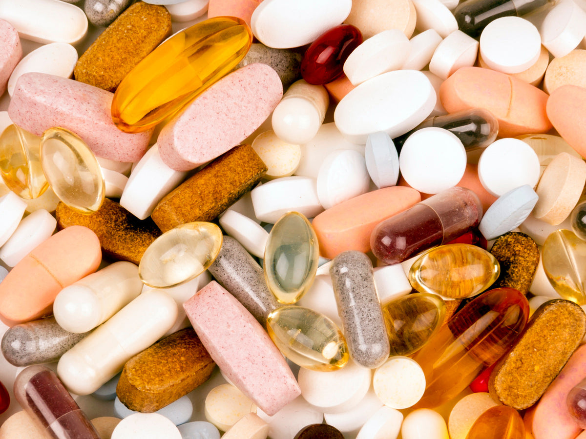 A close-up of a colorful assortment of different pills, tablets, and softgel capsules in various shapes and sizes, scattered together as a background.