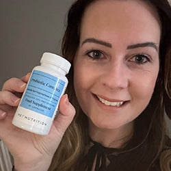 Smiling woman holding a bottle of Hey Nutrition Probiotic Complex, with the label visible reading "Probiotic Complex, Suitable for Vegetarians & Vegans, 20 Billion CFU per Serving, Food Supplement, 60 Capsules."
