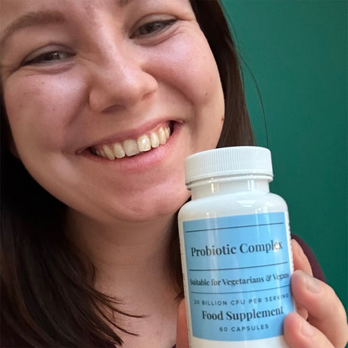 Smiling woman holding a bottle of Hey Nutrition Probiotic Complex, showing the front label that reads "Probiotic Complex, Suitable for Vegetarians & Vegans, 20 Billion CFU per Serving, Food Supplement, 60 Capsules."