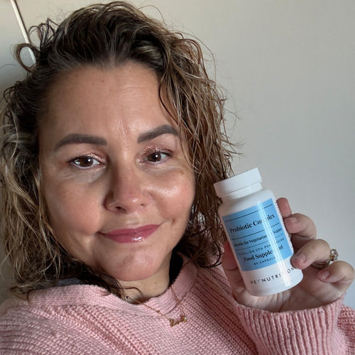 Woman in a pink sweater holding a bottle of Hey Nutrition Probiotic Complex, with the label clearly visible showing "Probiotic Complex, Suitable for Vegetarians & Vegans, 20 Billion CFU per Serving, Food Supplement, 60 Capsules."