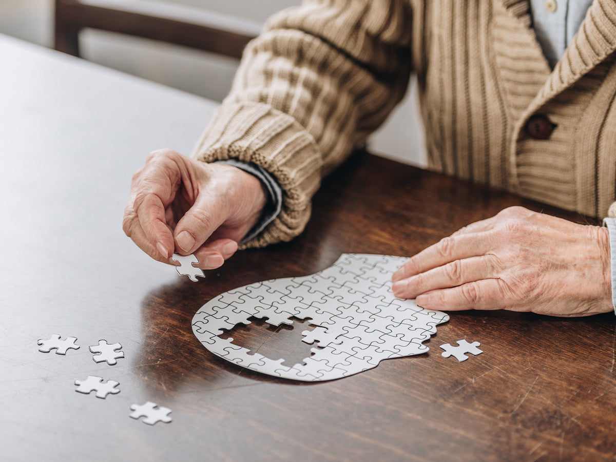 An elderly person working on a puzzle shaped like a human head, symbolizing memory and cognitive health.