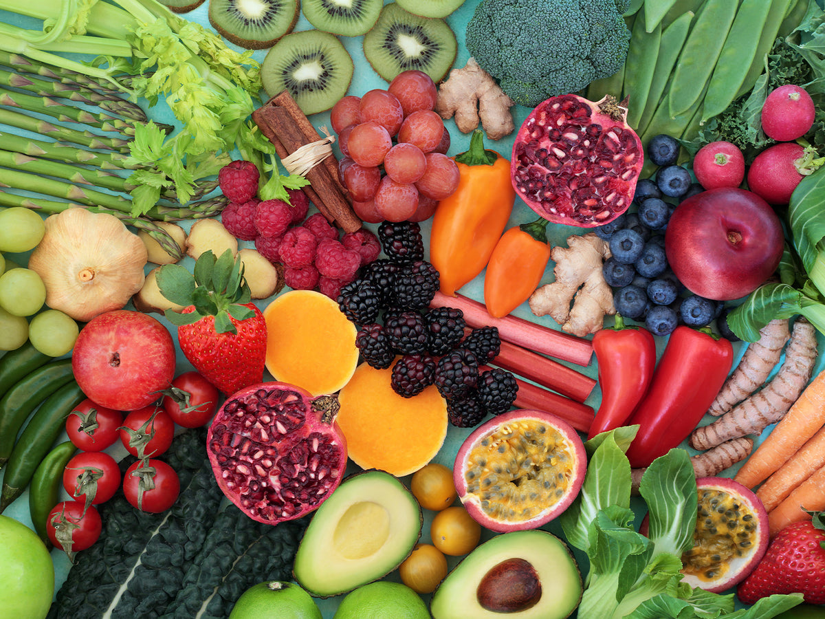 "Fresh assortment of colorful fruits and vegetables including pomegranate, avocado, grapes, tomatoes, carrots, peppers, berries, broccoli, kiwi, and leafy greens, symbolizing natural sources of vitamins and minerals."