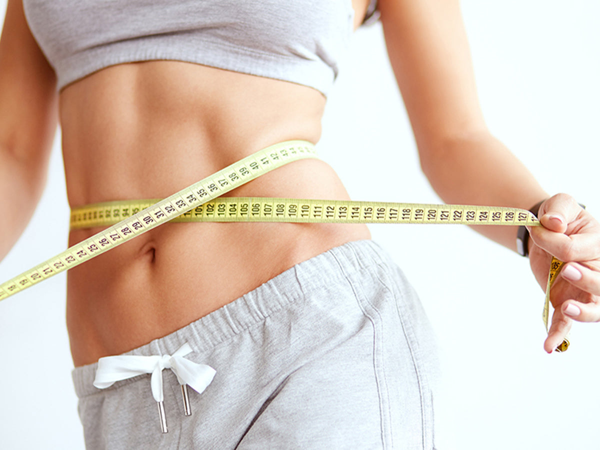 Person measuring slim waist with a yellow tape measure, symbolizing healthy weight management.