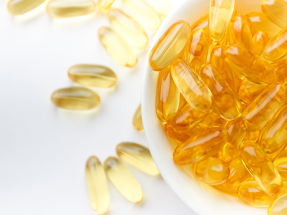 Fish oil softgels in a white bowl – A white bowl filled with translucent golden Omega 3 fish oil softgels, with several capsules scattered around, highlighting purity and potency.