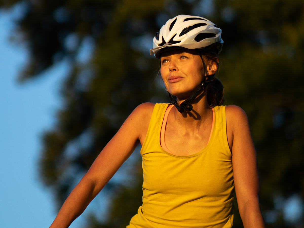 Cyclist in sunlight – A woman wearing a yellow tank top and white helmet looks upwards while cycling outdoors in the evening sun.