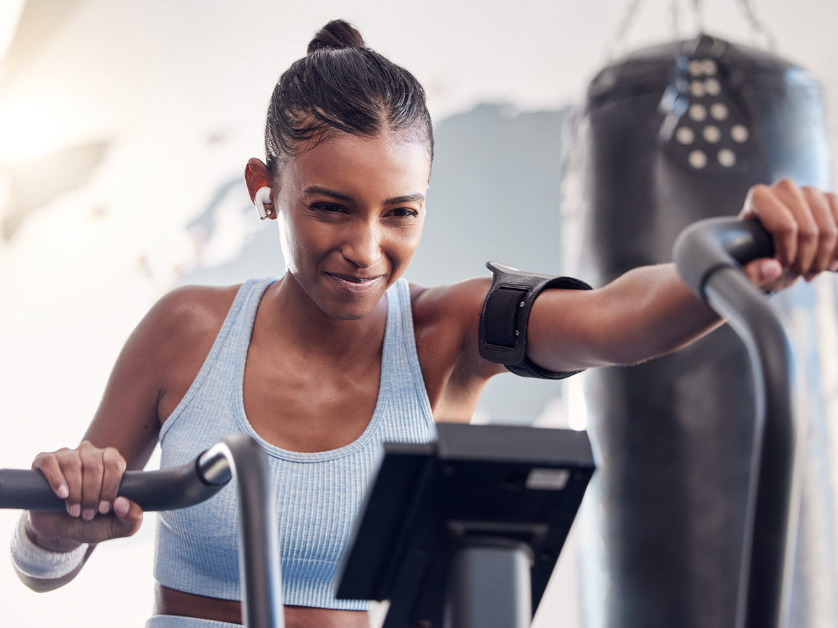 Woman working out on a stationary bike, wearing a blue sports bra and earbuds, smiling with determination while exercising.