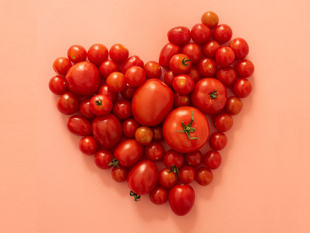 Assorted tomatoes arranged into a heart shape on a peach surface, symbolising heart-friendly, plant-based nutrition and lifestyle choices that complement cholesterol support from a dedicated, routine supplement regimen.