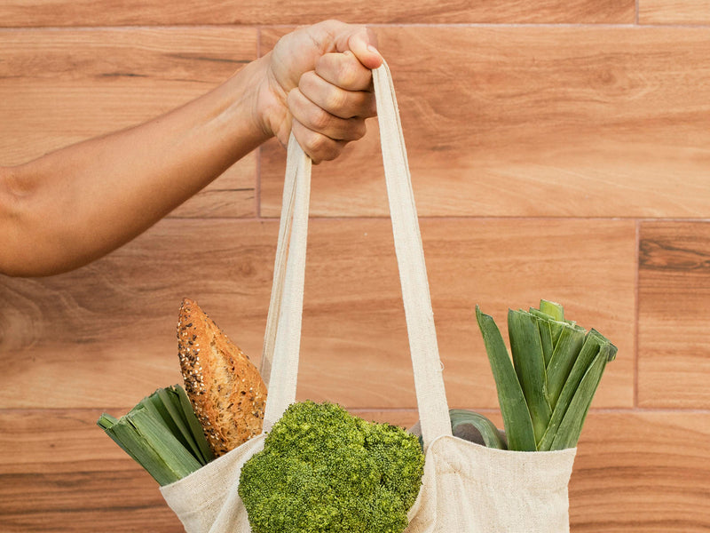 A hand holding a tote bag with vegetables in it.